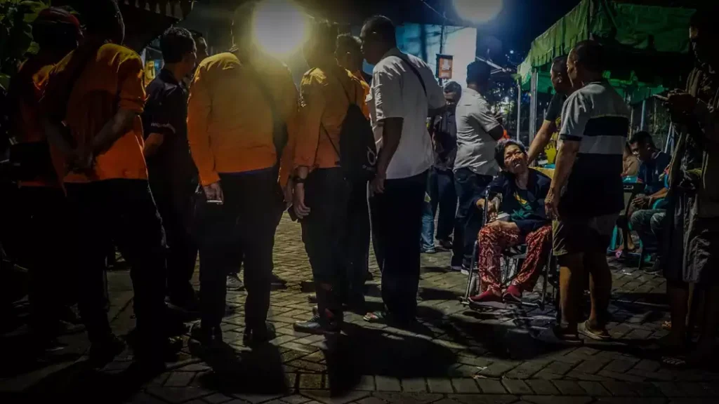 Seorang lansia tengah terduduk di kursi roda, ditemani sanak keluarga yang sedang bingung akan kondisi sedang mereka alami. Sementara, sejumlah petugas BPBD Kota Surabaya berkoordinasi untuk pendataan warga penghuni Gedung Setan yang terpaksa mengungsi akibat atap bangunan tua itu roboh dimakan usia.